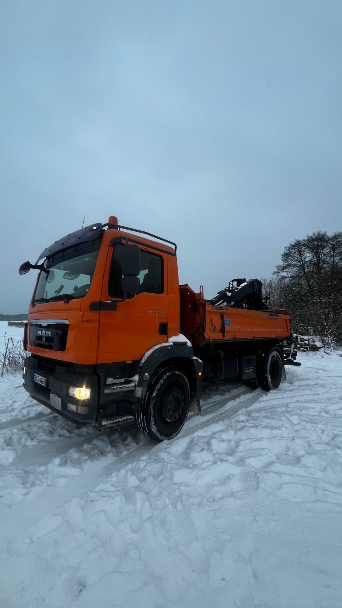 Zunk-Fahrzeug im Winterbetrieb Oranger Zunk-LKW mit Ladekran steht auf einer schneebedeckten Fläche